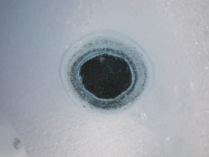A bird's eye view of a single cryoconite hole on the Greenland ice sheet. the hole is ca. 15cm wide and 20cm deep. The dark sediment on the hole floor provides a habitat for abundant microbial life and significant surface darkener!